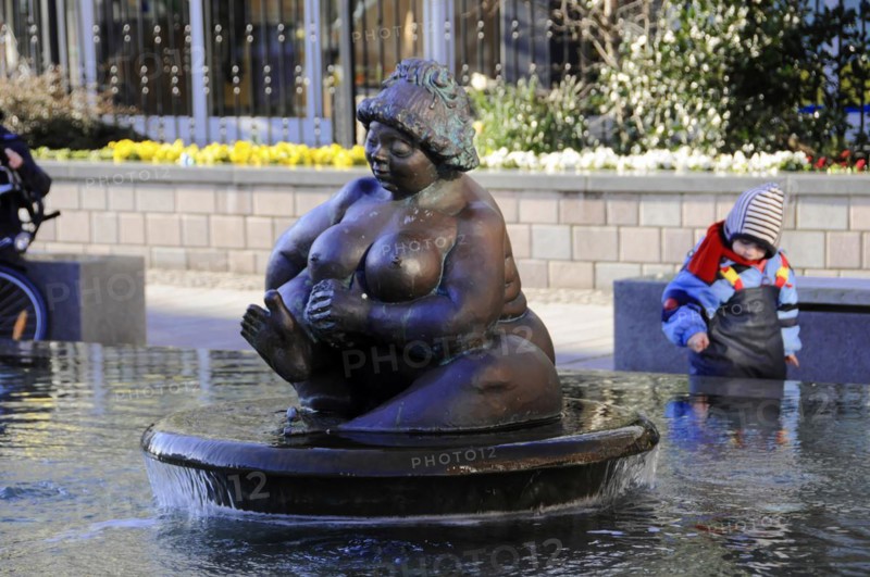 Fountain figure Wilhelmine, landmark of Westerland, Westerland, bronze sculpture of a seated woman in a fountain, a child playing in the background, Sylt, North Frisian Island, Schleswig Holstein, Germany, Europe