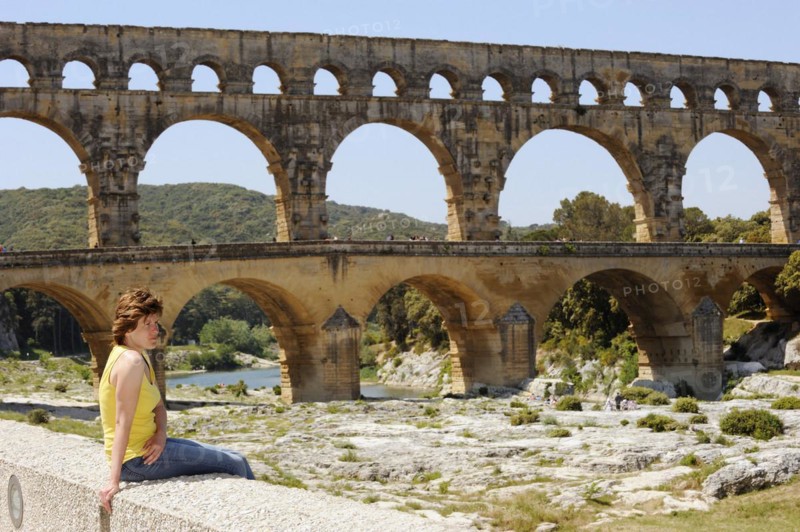 Woman sitting on a wall in front of the Pont du Gard, Roman aqueduct over the river Gardon, Vers-Pont-du-Gard, Languedoc-Roussillon, South of France, France, Europe