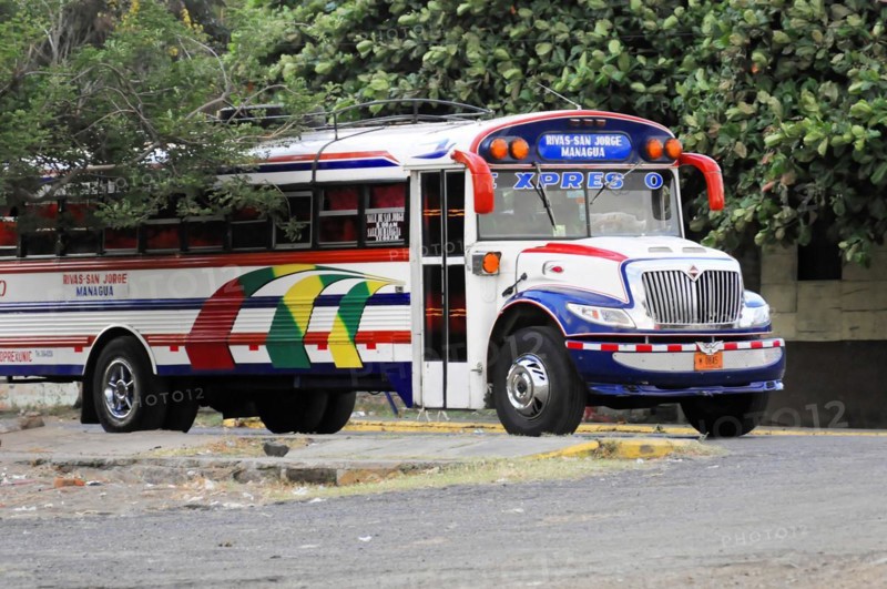 On the road near Rivas, Ometepe Island, Nicaragua, Parked colourful city bus surrounded by trees on a quiet stretch of road, Central America, Central America