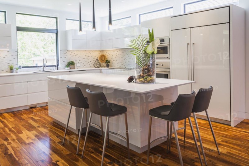 White high-gloss lacquered cabinets and island with grey leather bar stools and white quartz countertops in kitchen with acacia wood floorboards inside contemporary home, Quebec, Canada, North America