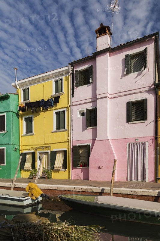 Moored boats on canal lined with pink, yellow and green stucco houses decorated with striped curtains over entrance doors and windows plus clothes on clothesline, Burano Island, Venetian Lagoon, Venice, Veneto, Italy, Europe