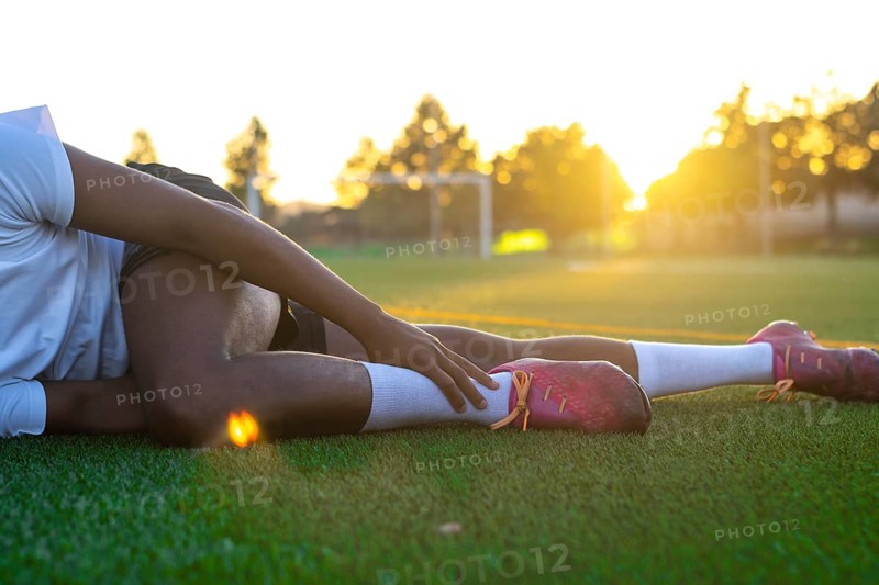 Football player with leg pain on the field. Football player lying on the grass rubbing his leg. Male football player lying on the grass rubbing his foot