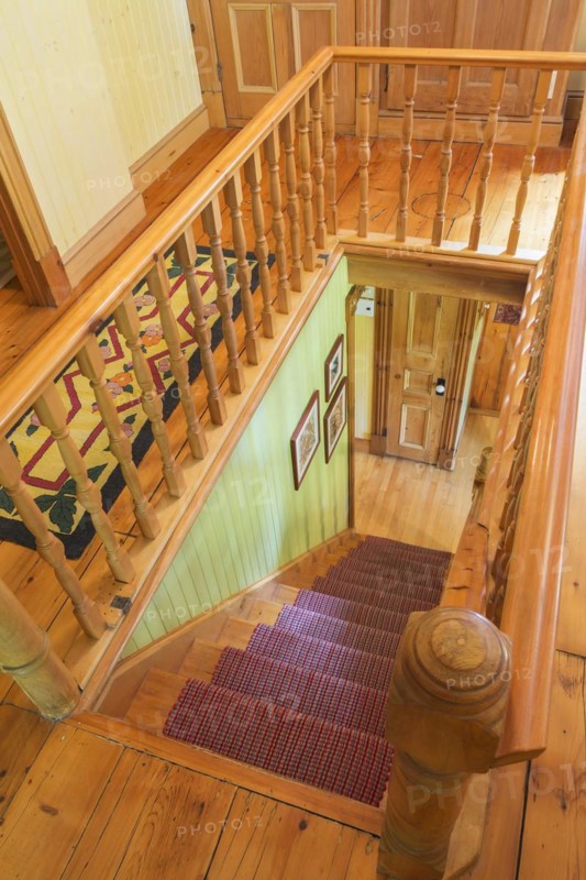 Looking down staircase with maple wood railings and pine wood steps covered with multi-coloured checkered rug runner inside an old circa 1850 Canadiana style house, Quebec, Canada, North America