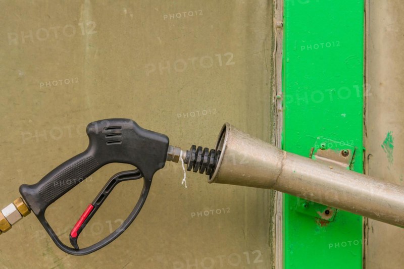 Black handle of car wash high pressure water gun with long nozzle inserted into metal cylinder in South Korea