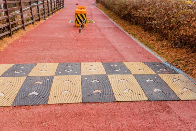 Yellow and black rubber speed bump across red asphalt bicycle path with traffic bollards slightly blurred in background in South Korea