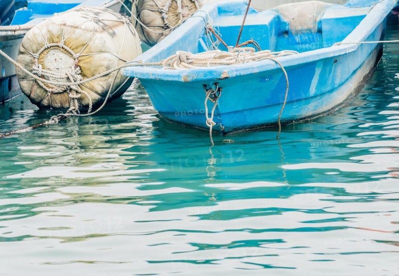 Closeup of small blue fishing boat floating in water tied to a large white buoy in South Korea