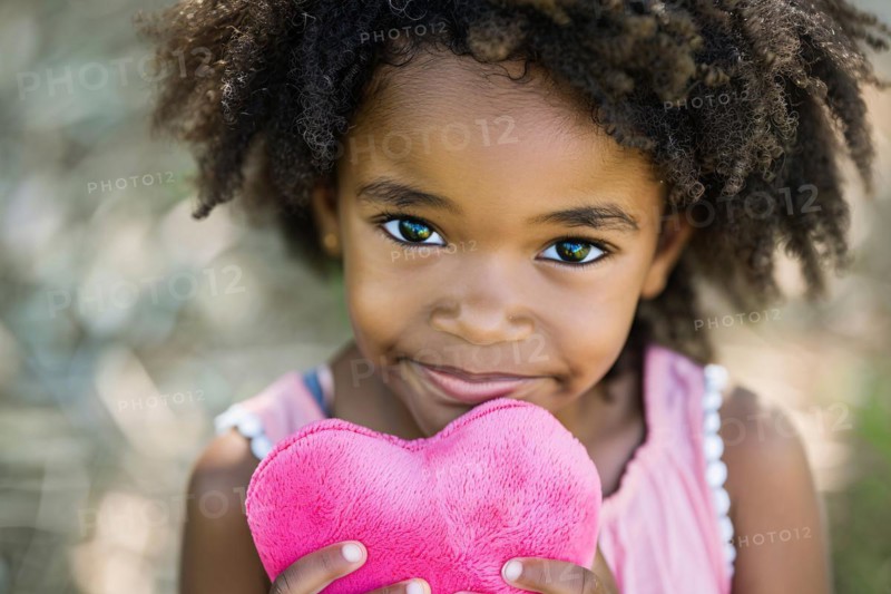 Young black girl child holding pink plush heart. KI generiert, generiert, AI generated