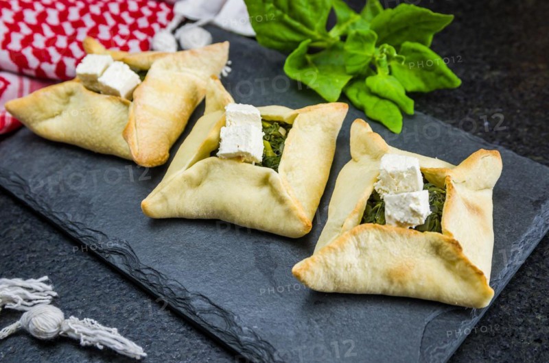 Delicious Lebanese (Arabic) food, spinach sfiha with ricotta cheese on a black slate stone background and traditional Lebanese turban Keffiyeh
