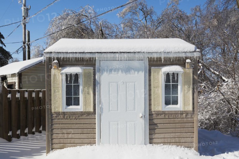 Storage shed facade covered in thick ice and snow in residential backyard after ice storm in early spring, Quebec, Canada, North America