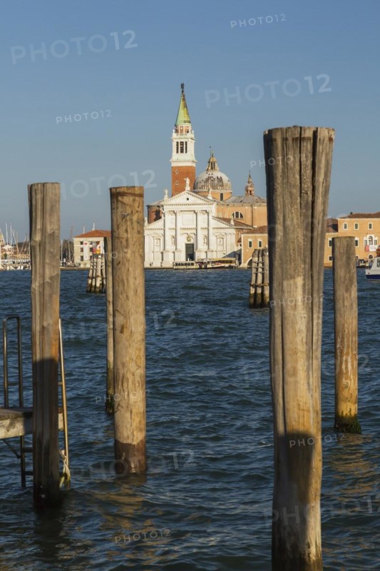 Wooden mooring posts canal lane markers in Venetian lagoon and 16th century Benedictine church of San Giorgio Maggiore with bell tower on San Giorgio Maggiore Island, Venice, Veneto, Italy, Europe