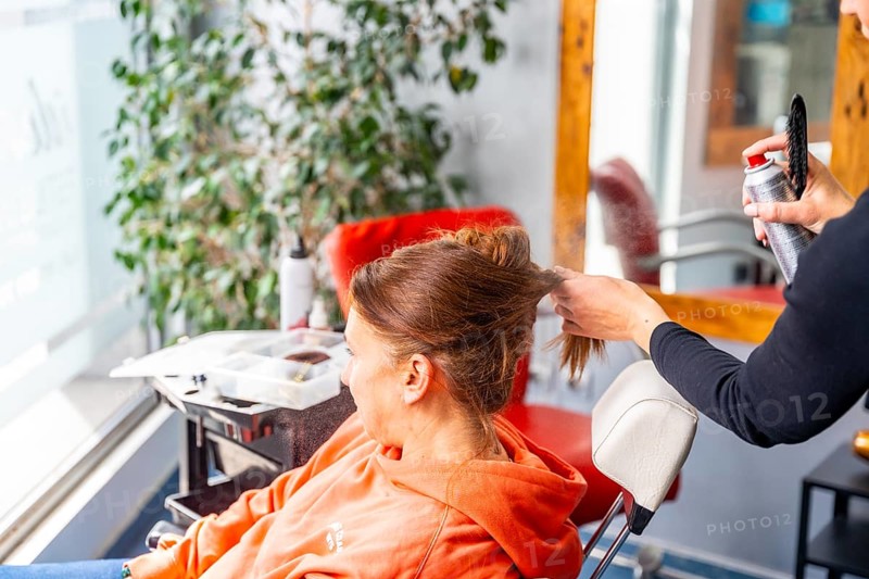 Unrecognizable female hairdresser applying hairspray to a client's hair in the salon