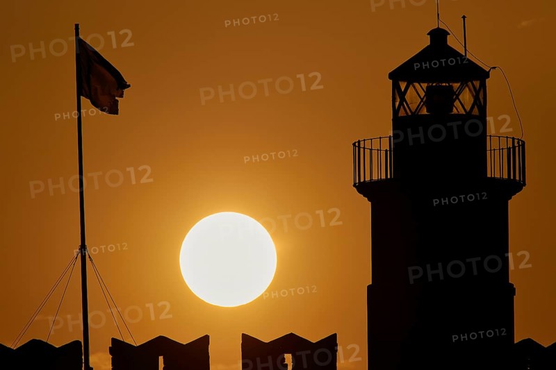 The silhouette of a lighthouse with a flag against the background of a round sunrise, sunrise, dawn, Fort of Saint Nikolaos, harbour promenade, Rhodes, Dodecanese, Greek Islands, Greece, Europe