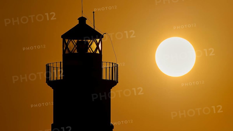 A lighthouse stands as a dark silhouette next to the round sun at sunrise, sunrise, dawn, Fort of Saint Nikolaos, harbour promenade, Rhodes, Dodecanese, Greek Islands, Greece, Europe