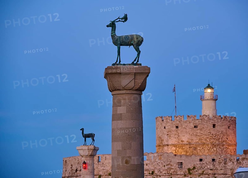 Deer statue on a pillar in front of a fortress wall and a lighthouse at dusk, Deer statue, Deer statue, Fort Agios Nikolaos, Mandraki harbour, European roe deer, Rhodes, Dodecanese, Greek Islands, Greece, Europe
