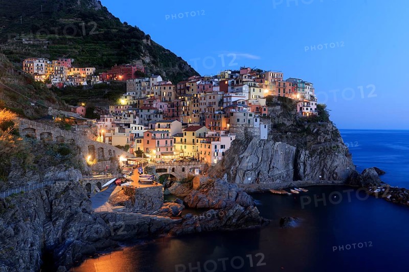 A Mediterranean village on the coast is romantically illuminated by the sea at nightfall, Italy, Liguria, Manarola, Riomaggiore, La Spezia Province, Cinque Terre, Europe