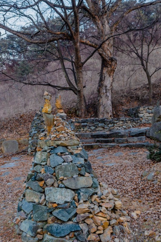 Upside down cone shaped tower of rocks and stones in rural roadside park on winter evening in South Korea