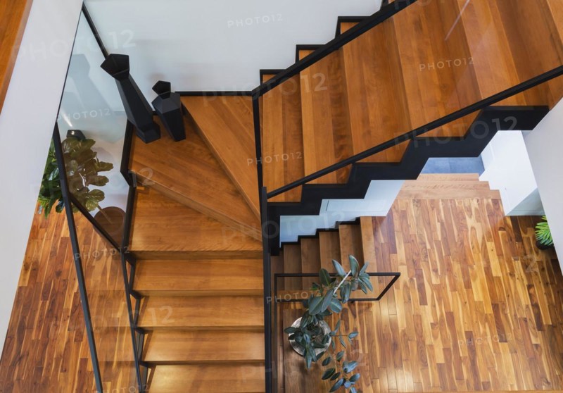 Top view of black powder coated steel L-shaped staircase with stained and varnished wooden steps and tempered glass handrail inside contemporary home with acacia wood flooring, Quebec, Canada, North America