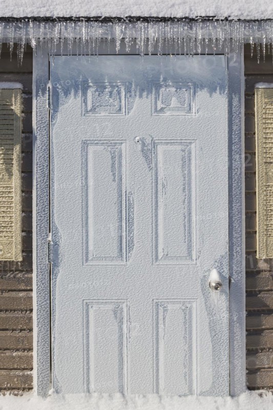 Storage shed door covered in thick ice and snow in residential backyard after ice storm in early spring, Quebec, Canada, North America