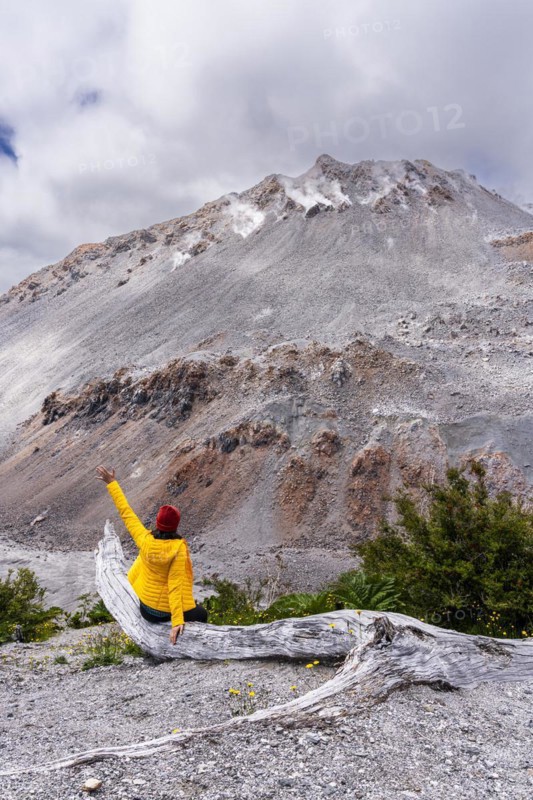 Young woman in yellow jacket sits in front of a volcano, Chaiten Volcano, Carretara Austral, Chile, South America