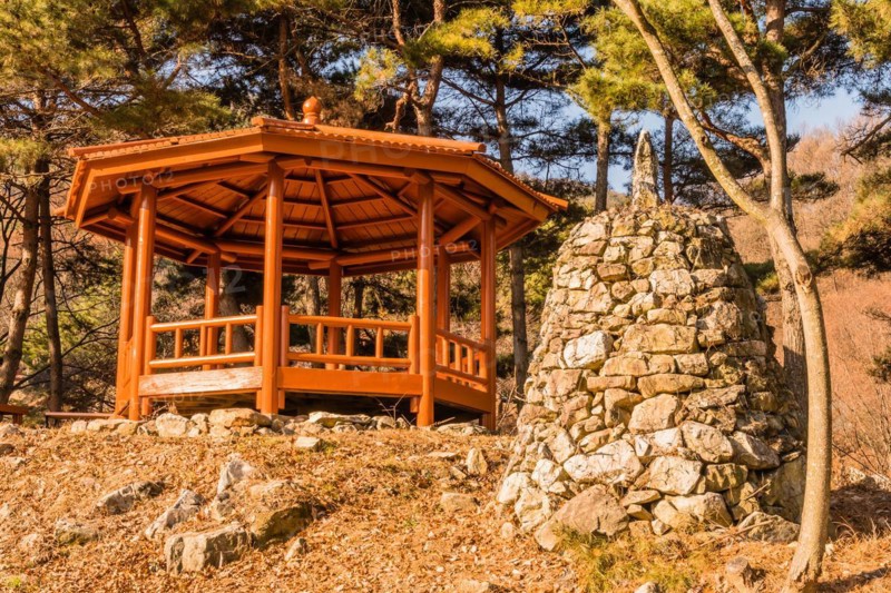 Stone pyramid next to wooden gazebo on small hill under grove of evergreen trees located in public mountain park in Yesan, South Korea, Asia
