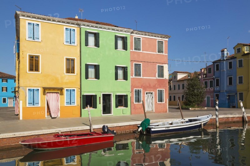 Moored boats on canal lined with orange, green and pink stucco houses decorated with striped curtains over entrance doors, Burano Island, Venetian Lagoon, Venice, Veneto, Italy, Europe