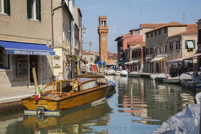 Moored boats on canal with colourful residential buildings, houses, shops, tourists and clock tower in San Stefano square, Murano Island, Venice Lagoon, Veneto, Italy, Europe