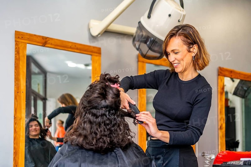Hairstylist ironing the hair of a client in a salon next to a mirror with image reflected on it