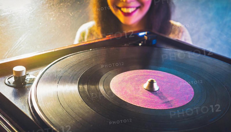 Stylish young lady with headphones chooses a track on a vintage record player in front of a colorful backdrop ai generated, AI generated