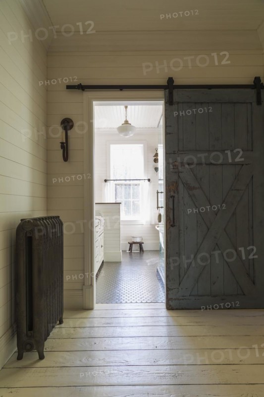 Kid's upstairs floor bathroom with distressed barn wood door, black honeycomb ceramic tile floor, white antique style finish cabinet, freestanding claw foot bathtub inside country style home, Quebec, Canada, North America