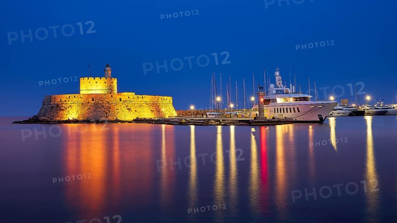 Historic castle with lighthouse at night, reflecting in the water next to a yacht, night shot, Fort of Saint Nikolaos, harbour promenade, Rhodes, Dodecanese, Greek Islands, Greece, Europe
