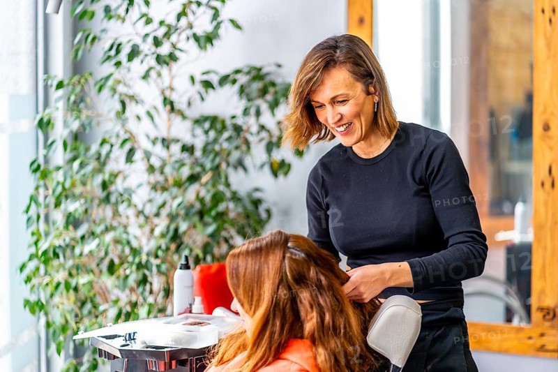 Side view photo with copy space of a smiling hairstylist attending a woman sitting in the hair salon