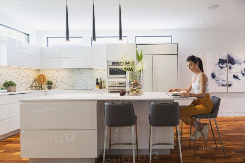 Interior designer Liza Castro in her kitchen with white high-gloss lacquered cabinets and island with grey leather bar stools and white quartz countertops and acacia wood floorboards inside contemporary home, Quebec, Canada, North America