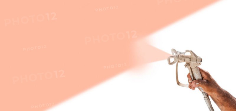 Professional spray painter holding spray gun spraying peach fuzz PMS color of the year 2024 over white surface