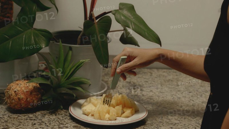 A hand poking a piece of chopped pineapple pieces on a plate with a fork for a healthy vegan summer snack