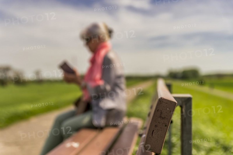 Senior citizen sitting on a bench and looking at her smartphone, side view, blurred, dike crest, Rhine, Zons, North Rhine-Westphalia, Germany, Europe