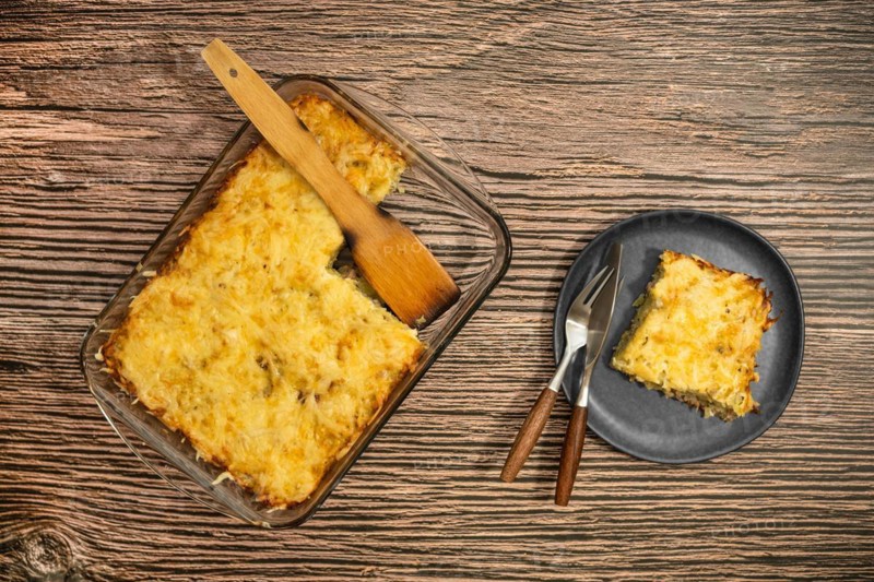 Top view of pie with meat and potato baked in oven in glass baking tray and on a plate
