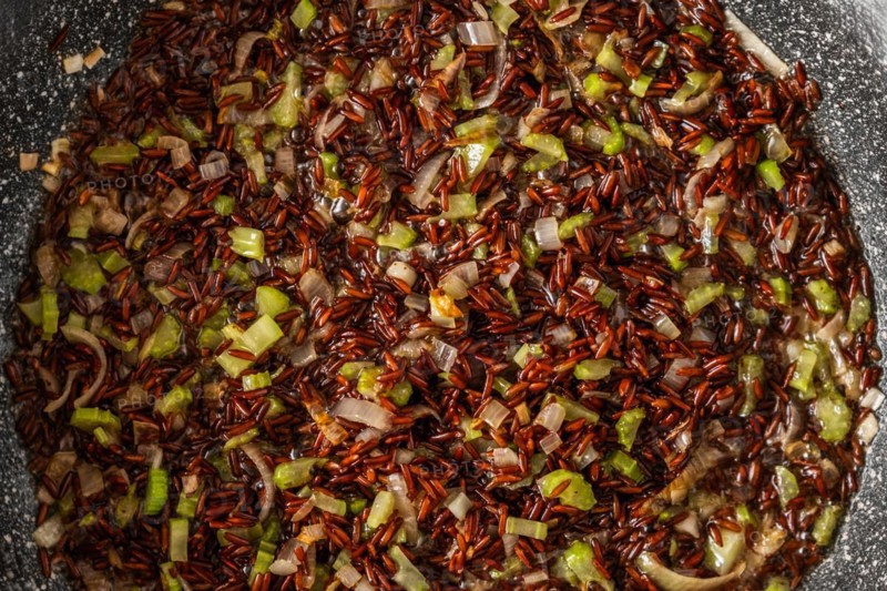 Closeup top view of frying pan with pink rice, onion and celery