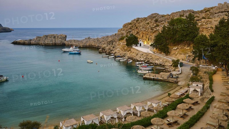 Bay with sun loungers and clear water, St Paul's Chapel, Paul's Bay, below the Acropolis of Lindos, Lindos, Rhodes, Dodecanese, Greek Islands, Greece, Europe