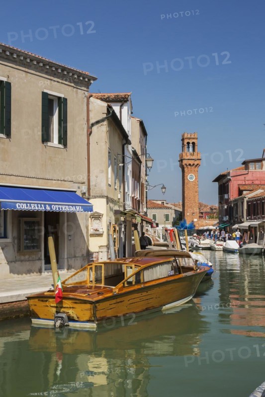 Moored boats on canal with colourful residential buildings, houses, shops, tourists and clock tower in San Stefano square, Murano Island, Venice Lagoon, Veneto, Italy, Europe
