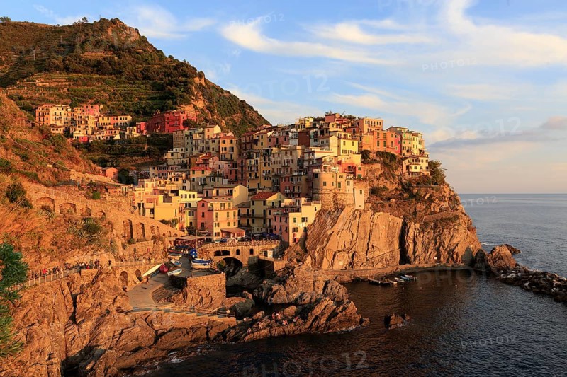 Morning sun shines on a colourful coastal town on the Italian Riviera with a view of the calm sea, Italy, Liguria, Manarola, Riomaggiore, La Spezia Province, Cinque Terre, Europe