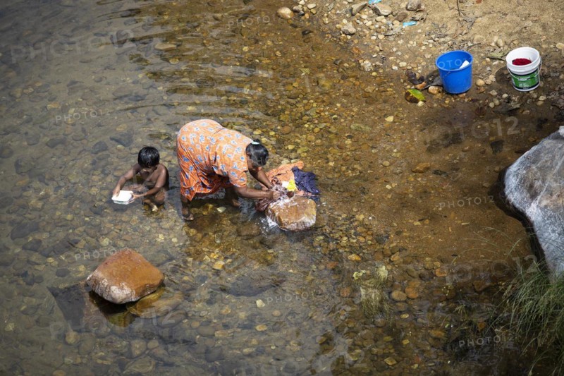 Indian woman washing clothes in the Periyar River, her son playing next to her, Mundakayam, Kerala, India, Asia