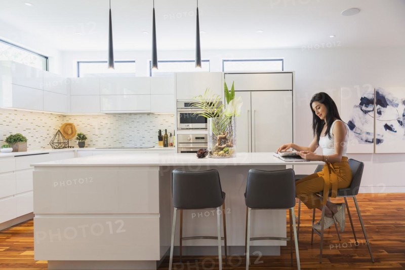 Interior designer Liza Castro in her kitchen with white high-gloss lacquered cabinets and island with grey leather bar stools and white quartz countertops and acacia wood floorboards inside contemporary home, Quebec, Canada, North America