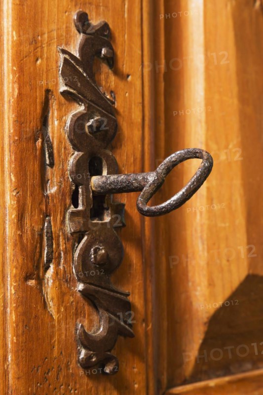 Close-up of antique metal key in keyhole of ornate door lock on wooden armoire in living room inside an old circa 1850 Canadiana style house, Quebec, Canada, North America