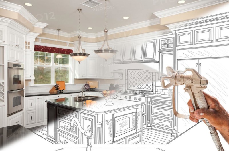 Professional spray painter holding spray gun spraying renovated kitchen over design drawing