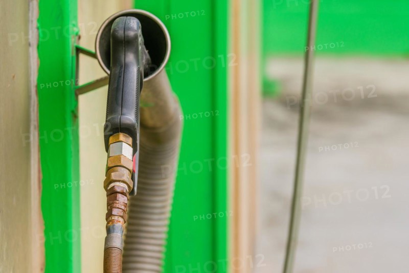 Rear view of black handle of car wash high pressure water gun with long nozzle inserted into metal cylinder in South Korea