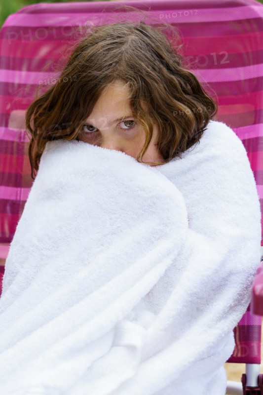 Pretty eight-year-old girl sitting on a chair wrapped in a white towel after getting out of the water, looking cold