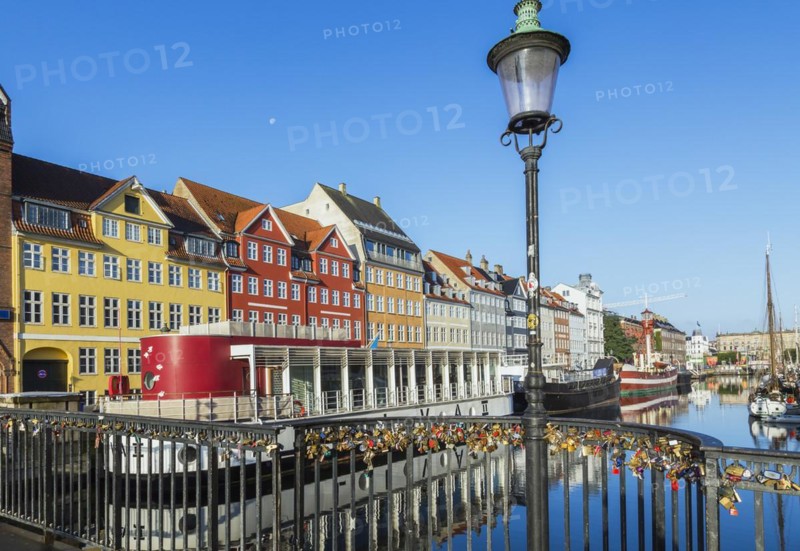 Love locks on black metal railing of canal bridge with antique lamppost, moored boats and colourful 17th century apartment buildings and houses, Nyhaven, Copenhagen, Denmark, Europe