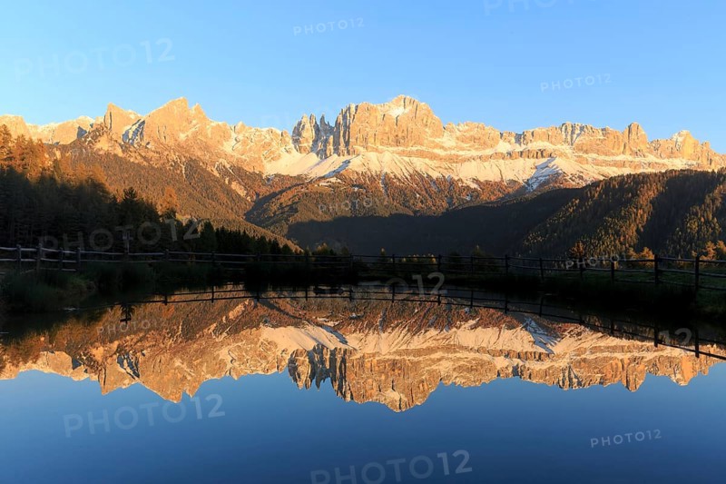 Sunrise behind the mountains with bright red colours reflected in the clear water of the lake, Trentino-Alto Adige, Alto Adige, Bolzano province, Dolomites, Reflection rose garden at Wuhnleger Lake, San Cipriano