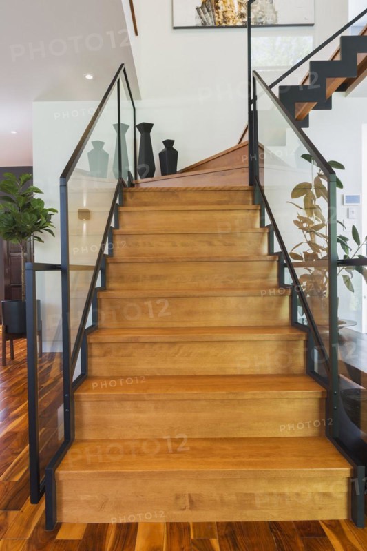 Black powder coated steel L-shaped staircase with stained and varnished wooden steps and tempered glass handrail inside contemporary home with acacia wood flooring, Quebec, Canada, North America