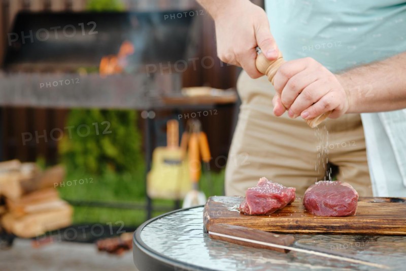 Unrecognizable man using hand mill to season raw strip steak with salt